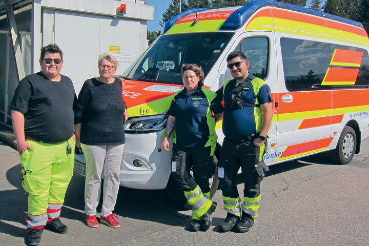 Ein ÖAMTC-Mitglied steht mit Sanitäter:innen vor einem Rettungsfahrzeug.