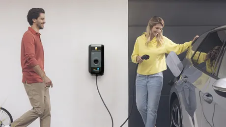 Eine Frau lädt ein Elektroauto vor einem Haus mit eigener Wallbox, ein Mann steht neben ihr.