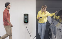 Eine Frau lädt ein Elektroauto vor einem Haus mit eigener Wallbox, ein Mann steht neben ihr.
