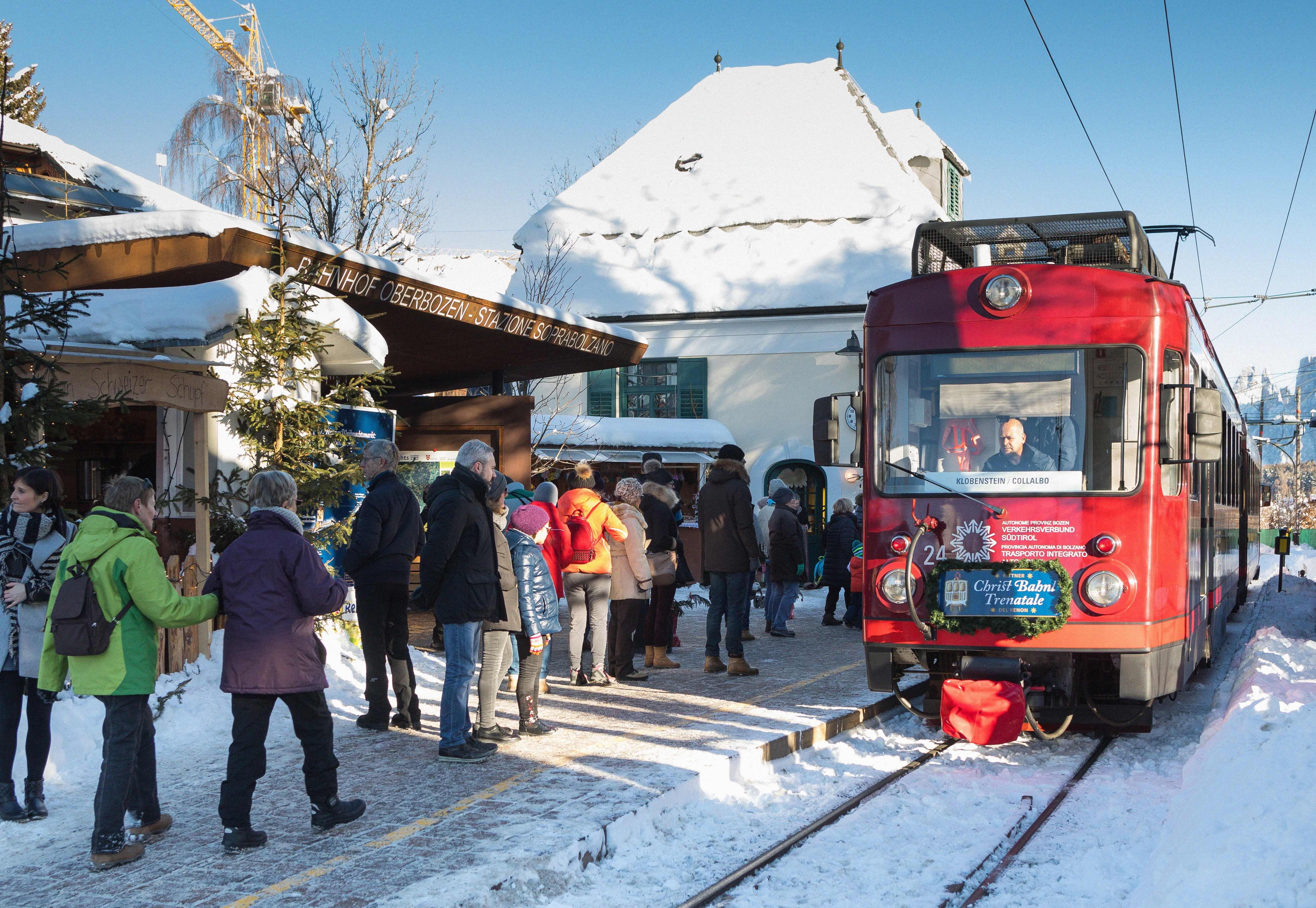 Menschen warten an einem verschneiten Bahnhof auf eine rote Straßenbahn.