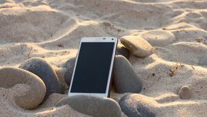 Smartphone liegt am Sandstrand zwischen Steinen.
