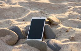 Smartphone liegt am Sandstrand zwischen Steinen.