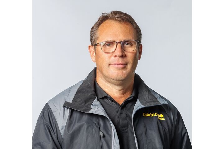 Das Bild ist ein Portrait von Roland Frisch, der frontal in die Kamera schaut und eine schwarze Jacke mit gelber ÖAMTC Fahrtechnik-Aufschrift trägt.