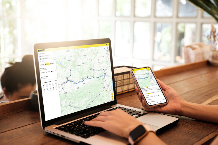 Eine Person nutzt einen Laptop und ein Smartphone mit der ÖAMTC-App zur Routenplanung.