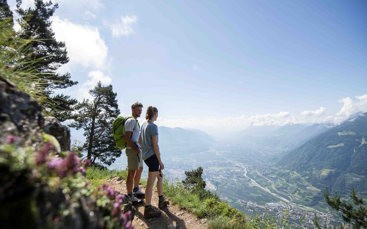 Das Foto zeigt ein Paar am Meraner Höhenweg im Sommer, die den Blick über das Parorama der Dolomiten schweifen lassen.