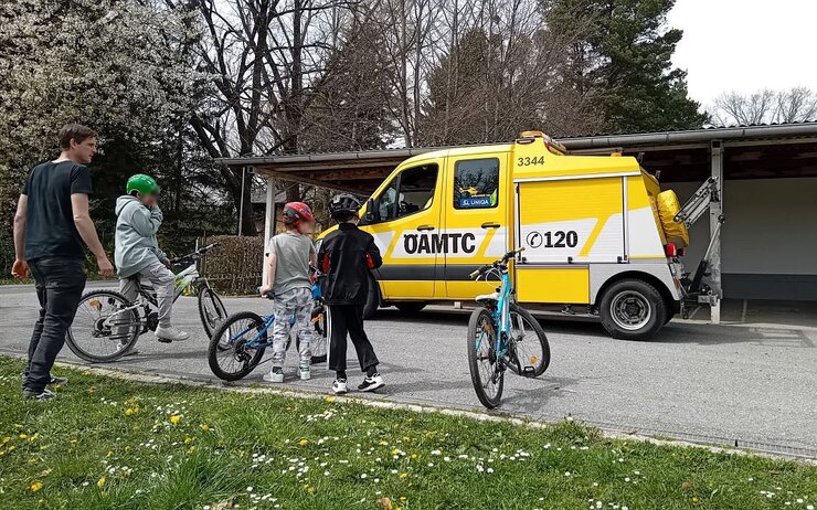 Kinder mit Fahrrädern und ein Erwachsener vor ÖAMTC Fahrzeug