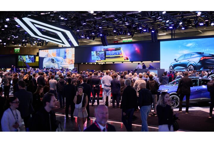 Viele Menschen auf einer Automesse vor einer Bühne mit Bildschirmen.