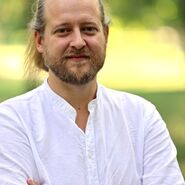 Das Bild ist ein Portraitfoto von Michael Szemes. Er trägt ein weißes Hemd und verschränkt die Arme. Der Hintergrund ist grün.