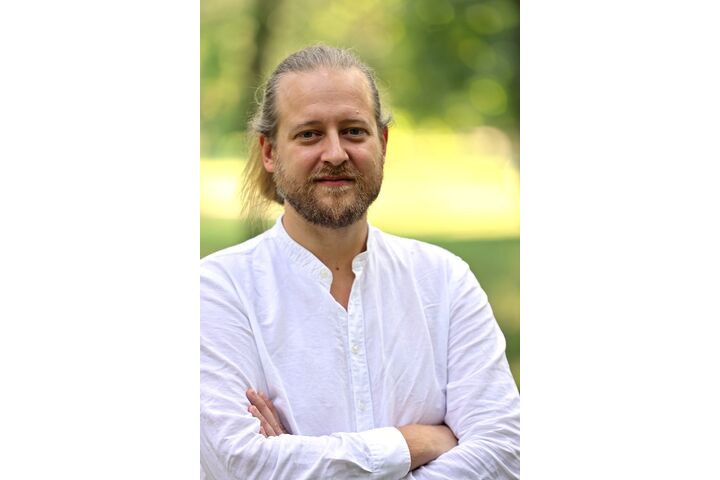 Das Bild ist ein Portraitfoto von Michael Szemes. Er trägt ein weißes Hemd und verschränkt die Arme. Der Hintergrund ist grün.