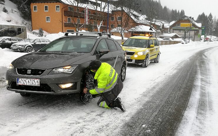Ein ÖAMTC Pannenfahrer legt bei einem Fahrzeug Schneeketten an.