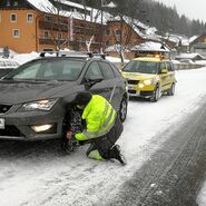Ein ÖAMTC Pannenfahrer legt bei einem Fahrzeug Schneeketten an.