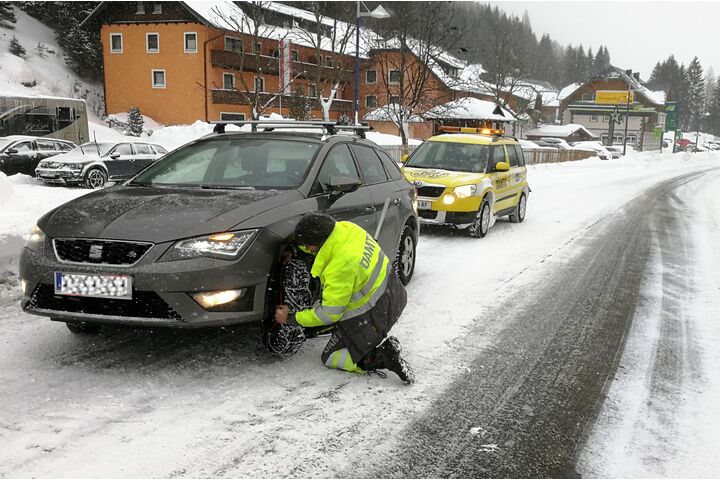 Ein ÖAMTC Pannenfahrer legt bei einem Fahrzeug Schneeketten an.
