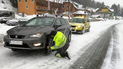 Ein ÖAMTC Pannenfahrer legt bei einem Fahrzeug Schneeketten an.