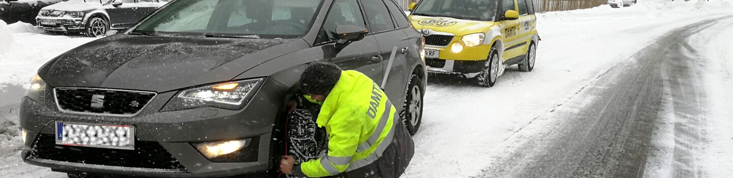 Ein ÖAMTC Pannenfahrer legt bei einem Fahrzeug Schneeketten an.