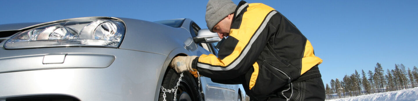Mann der Schneeketten am Fahrzeug anlegt.