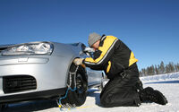 Mann der Schneeketten am Fahrzeug anlegt.