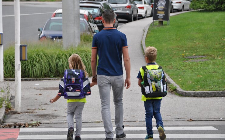 Eine erwachsene Person geht mit zwei Schulkindern über den Zebrastreifen.