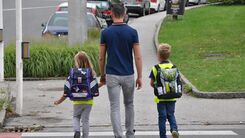 Eine erwachsene Person geht mit zwei Schulkindern über den Zebrastreifen.