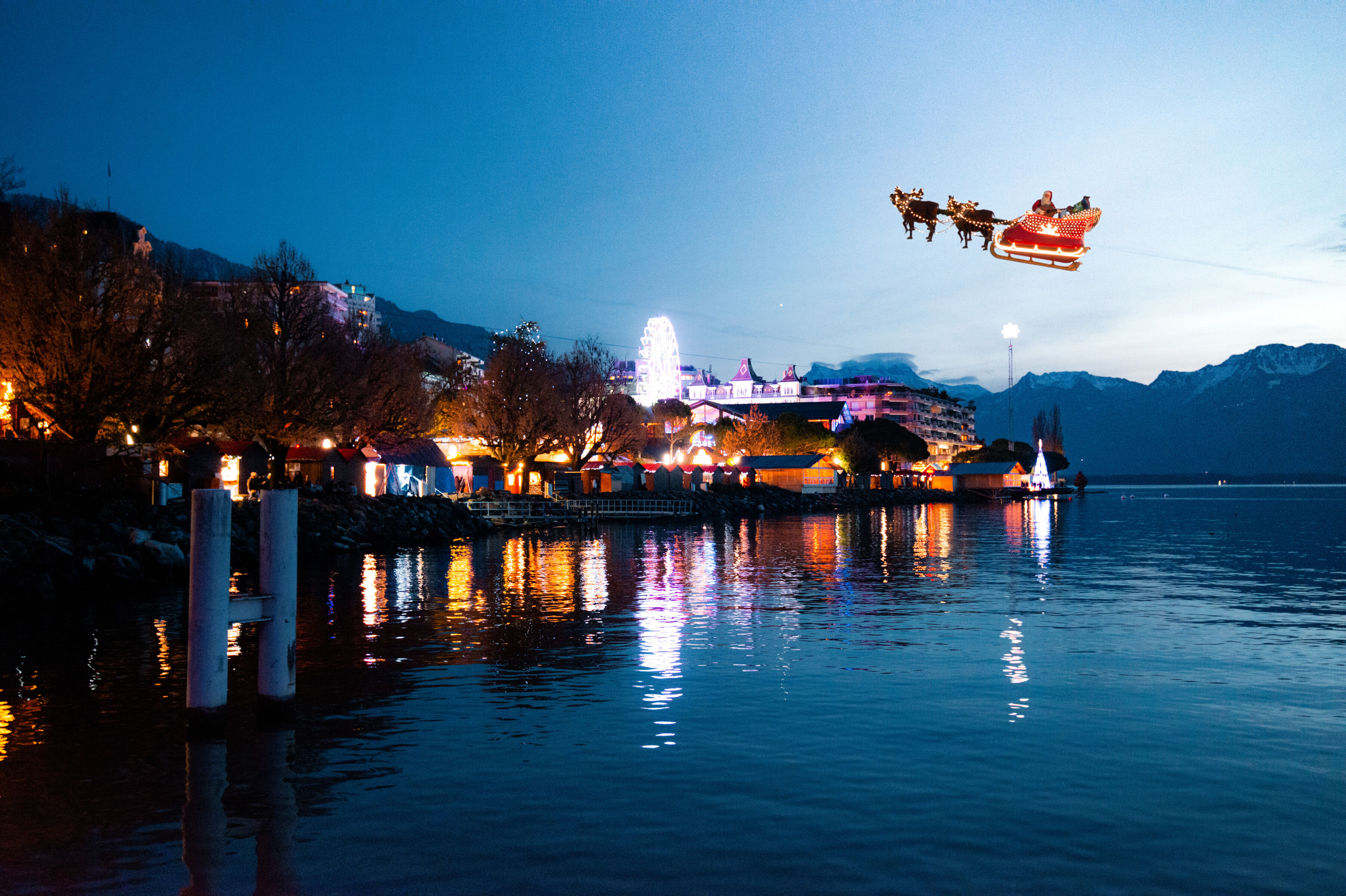 Eine weihnachtlich beleuchtete Stadt am Seeufer mit dem fliegenden Weihnachtsmannschlitten im Nachthimmel.