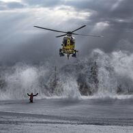 Snow Ein Christophorus-Hubschrauber wird in einer Schneelandschaft von einer Person zur Landung eingewiesen. Der Einweiser hält beide Arme nach oben