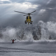 Ein Christophorus-Hubschrauber wird in einer Schneelandschaft von einer Person zur Landung eingewiesen. Der Einweiser hält beide Arme nach oben 