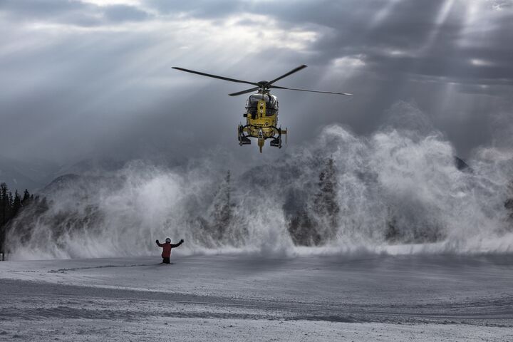 Ein Christophorus-Hubschrauber wird in einer Schneelandschaft von einer Person zur Landung eingewiesen. Der Einweiser hält beide Arme nach oben