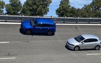 Ein blauer SUV und ein silberner Kleinwagen - Testautos für den Sommerreifentest 2022 - fahren hintereinander auf einer mehrspurigen Straße. Im Hintergrund sind Bäume und ein blauer Himmel zu sehen. 
