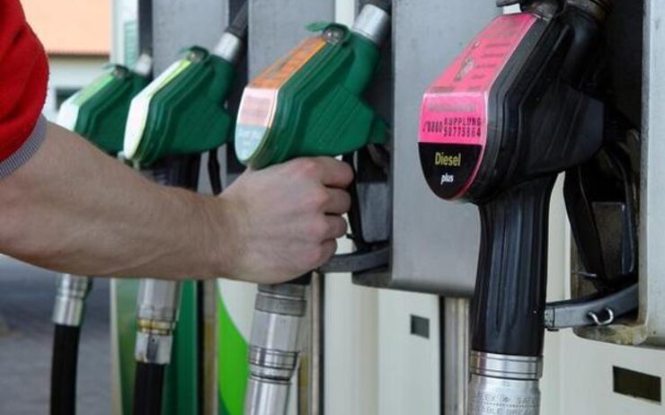 Eine Hand die nach der Zapfsäule auf der Tankstelle greift.