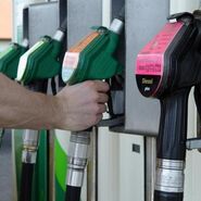 Eine Hand die nach der Zapfsäule auf der Tankstelle greift.