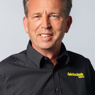 Porträt eines lächelnden Mannes mittleren Alters in einem schwarzen Hemd mit der Aufschrift "ÖAMTC Fahrtechnik"