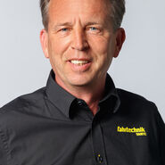 Porträt eines lächelnden Mannes mittleren Alters in einem schwarzen Hemd mit der Aufschrift "ÖAMTC Fahrtechnik"