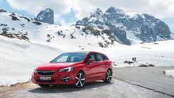 Das Foto zeigt ein rotes Fahrzeug vor verschneiten Bergen.