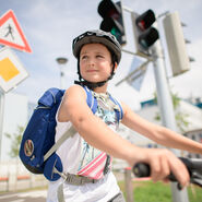 Ein Junge fährt auf einem Fahrrad. Er trägt einen Helm und eine blaue Schultasche am Rücken.