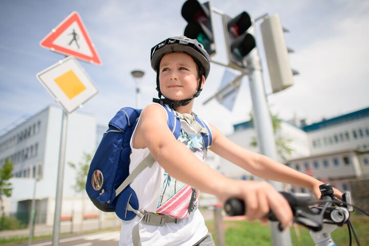 Ein Junge fährt auf einem Fahrrad. Er trägt einen Helm und eine blaue Schultasche am Rücken.