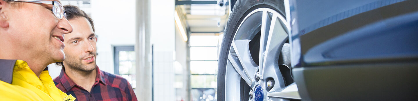 ÖAMTC Techniker und Mitglied begutachten die Profiltiefe eines Autos auf der Hebebühne