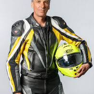 SCHEIBLAUER Georg Porträt eines Mannes mit grauem Haar in voller Motorradmontur mit einem Helm in der Hand