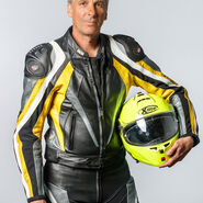 Porträt eines Mannes mit grauem Haar in voller Motorradmontur mit einem Helm in der Hand