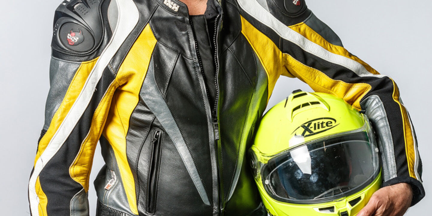 Porträt eines Mannes mit grauem Haar in voller Motorradmontur mit einem Helm in der Hand