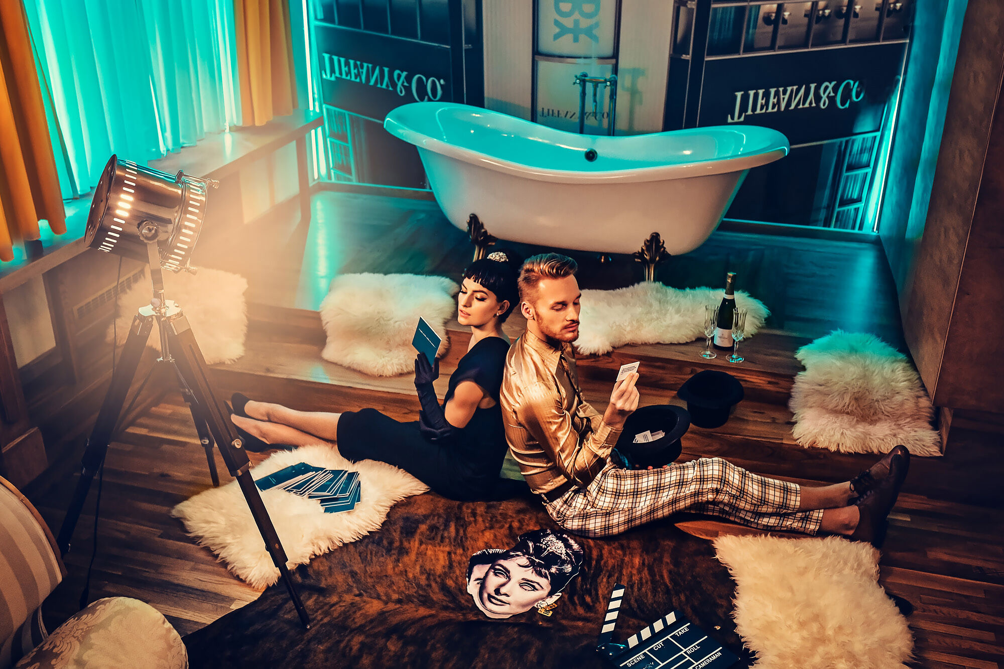 Ein Paar sitzt auf einem Teppich, umgeben von Filmrequisiten, mit einer Badewanne im Hintergrund.