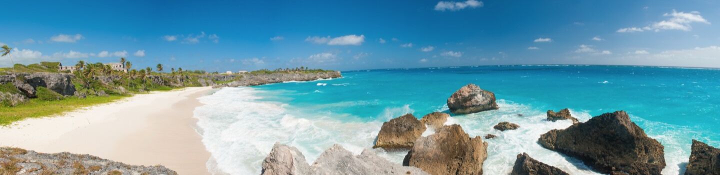 ruhige Küstenlinie mit einem weißen Strand, an dessen Vorderseite große Steine liegen, während das tiefblaue Meer sanfte, wellen mit weißem Schaum formt.