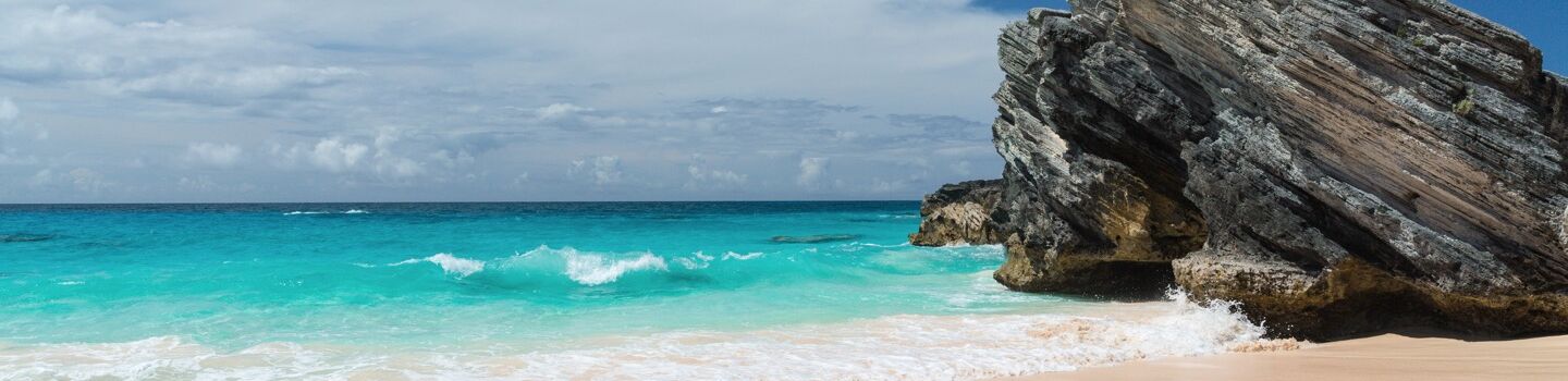  Traumhafter Strand mit kristallklarem blauen Wasser, das sanft an einen beeindruckenden großen Felsen rollt.
