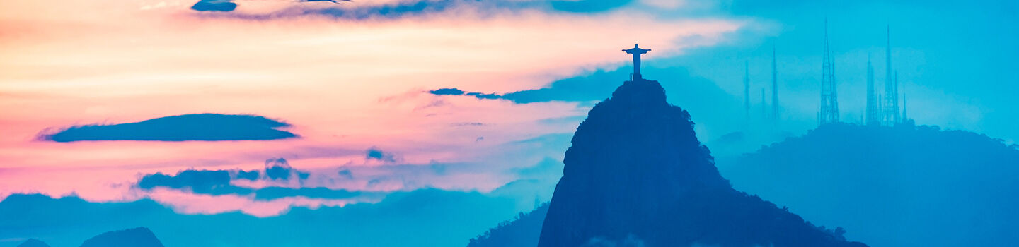 Im sanften Abendlicht zeichnet sich die Silhouette des Corcovado in Brasilien, mit der imposanten Cristo Redentor Statue, deutlich gegen den von Blau zu Gelb wechselnden Himmel ab.