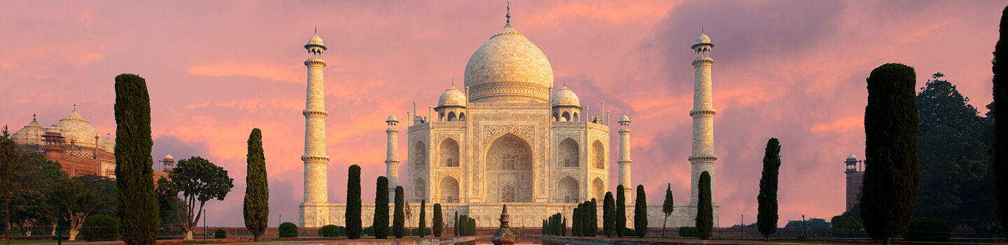 Ein riesiges weißes Marmor-Mausoleum mit Türmen und Kuppeln: das Taj Mahal, ein Wahrzeichen Indiens.