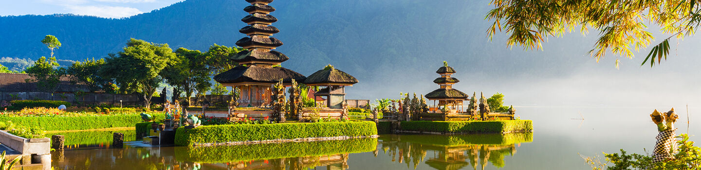 Ein buddhistischer Tempel mit hohem Turm an einem nebelverhangenen See, umgeben von einem prachtvollen Garten