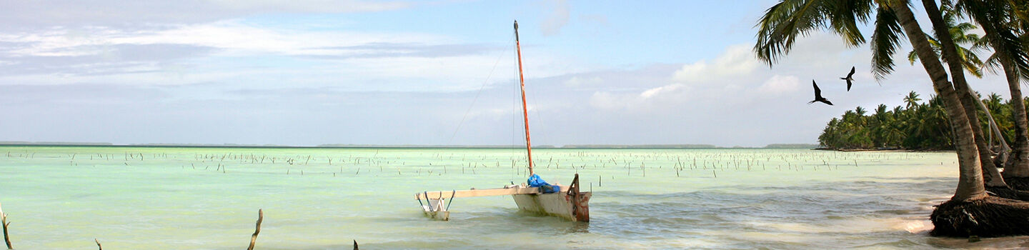 Tropischer Sandstrand mit Palmen, einem Boot und türkisblauem Wasser auf Fanning Island, Kiribati.