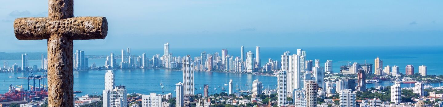 Das Kreuz von Cartagena in Kolumbien ragt stolz empor, wacht über eine Stadt, deren schneeweiße Hochhäuser an der glitzernden Meeresküste liegen.