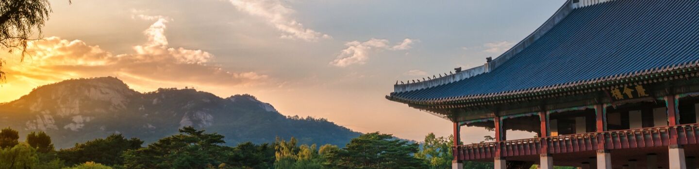Blick auf das Dach und die Säulen eines großen Tempels, im Hintergrund sind Bäume und ein Berg zu sehen