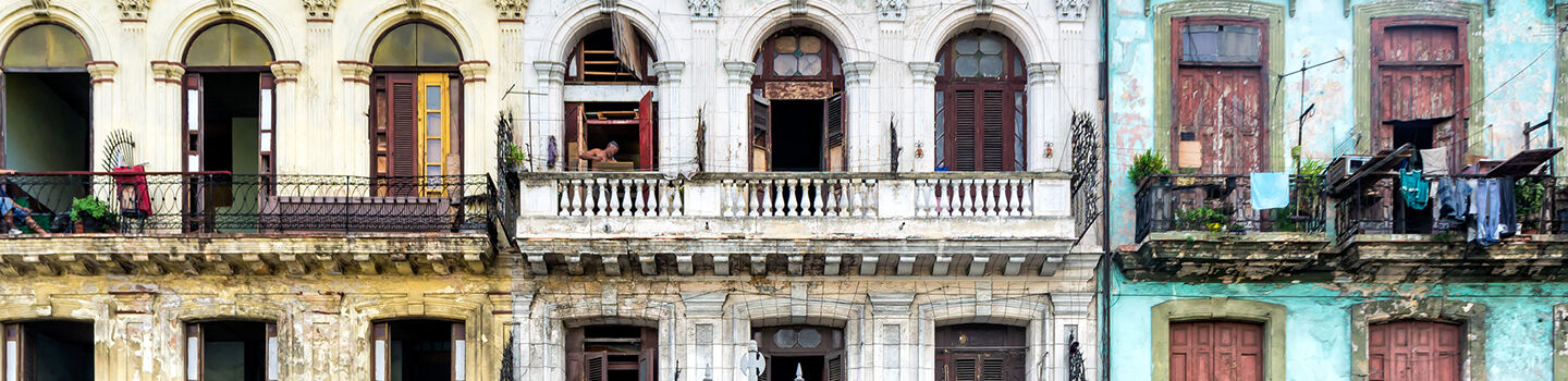 Drei pastellfarbene Häuser - in Gelb, Weiß und Türkis - mit hohen Fenstern und Balkonen.