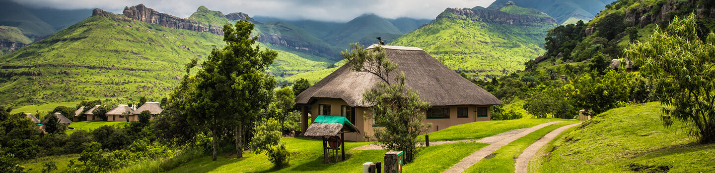 Blick auf die weitläufige Natur des Royal-Natal-Nationalparks, einschließlich einiger rustikaler Hütten mit Strohdächern
