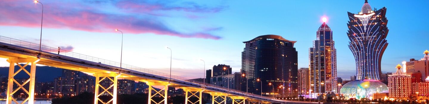 Beleuchtete Brücke in Macau, im Hintergrund Wolkenkratzer und Hochhäuser in Abendstimmung